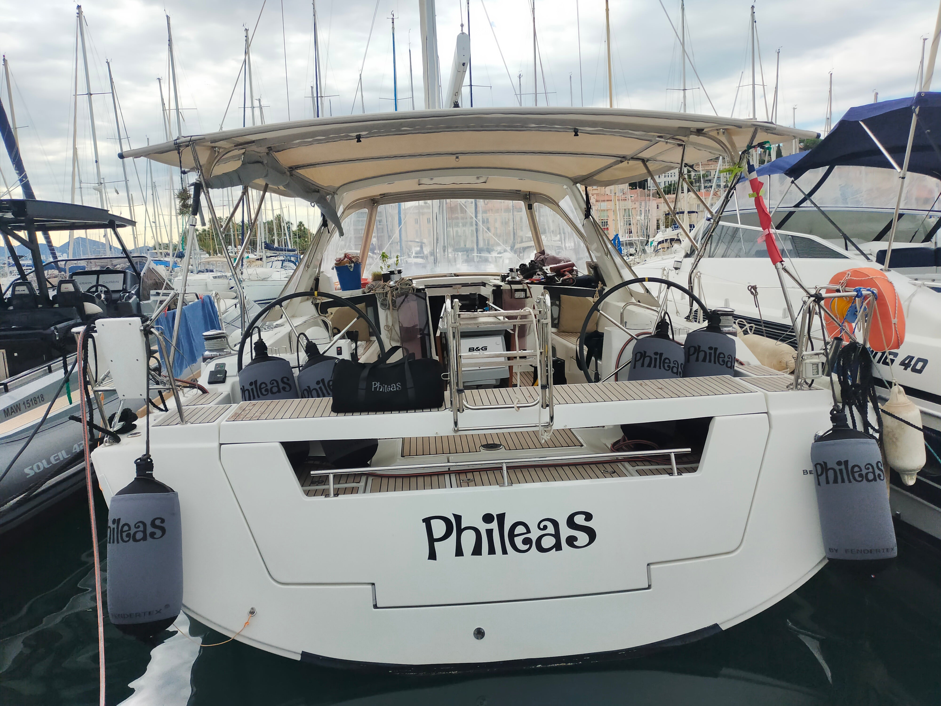 White sailboat named 'Phileas' docked among other boats on a cloudy day. Equiped with fendertex inflatable boat fenders.